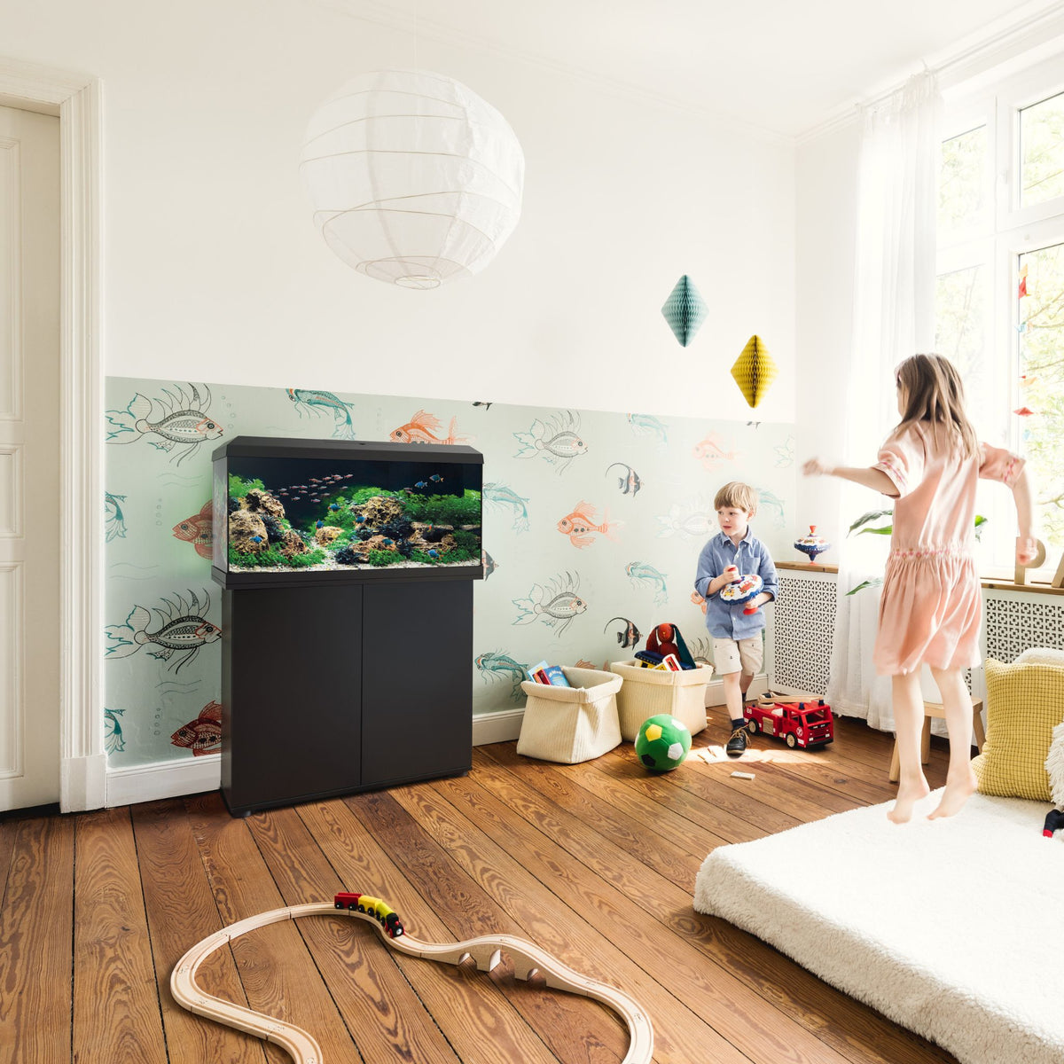Children playing in a nursery beside a black Juwel Primo aquarium on its cabinet