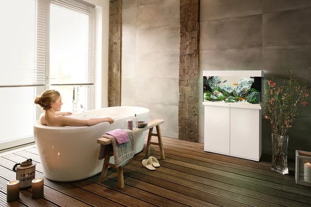 White Juwel RIO aquarium in a bathroom with a person relaxing in a freestanding bath