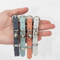 A hand holding all four Lilly and Dash cat collars, charcoal, sage, terracotta and cloud