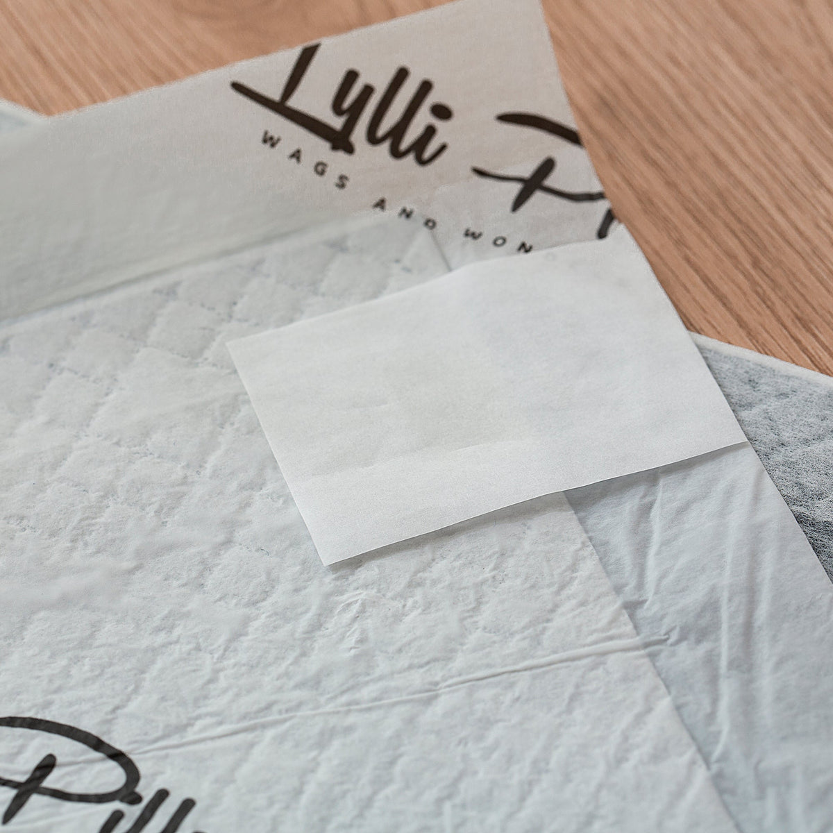 Close-up of a Lylli Pad on a timber floor showing the printed Lylli Pilly branding and a self-adhesive corner sticker