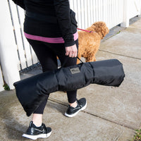 A person carrying a rolled Superior Pet Goods Rollup Pet Travel Mat while walking a dog