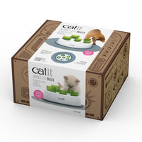Catit Senses 2.0 Food Digger with green tubes on a white base, a ginger cat pawing at it