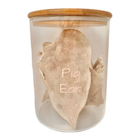 A single Freezy Paws freeze dried pig ear in a glass jar with a wooden lid