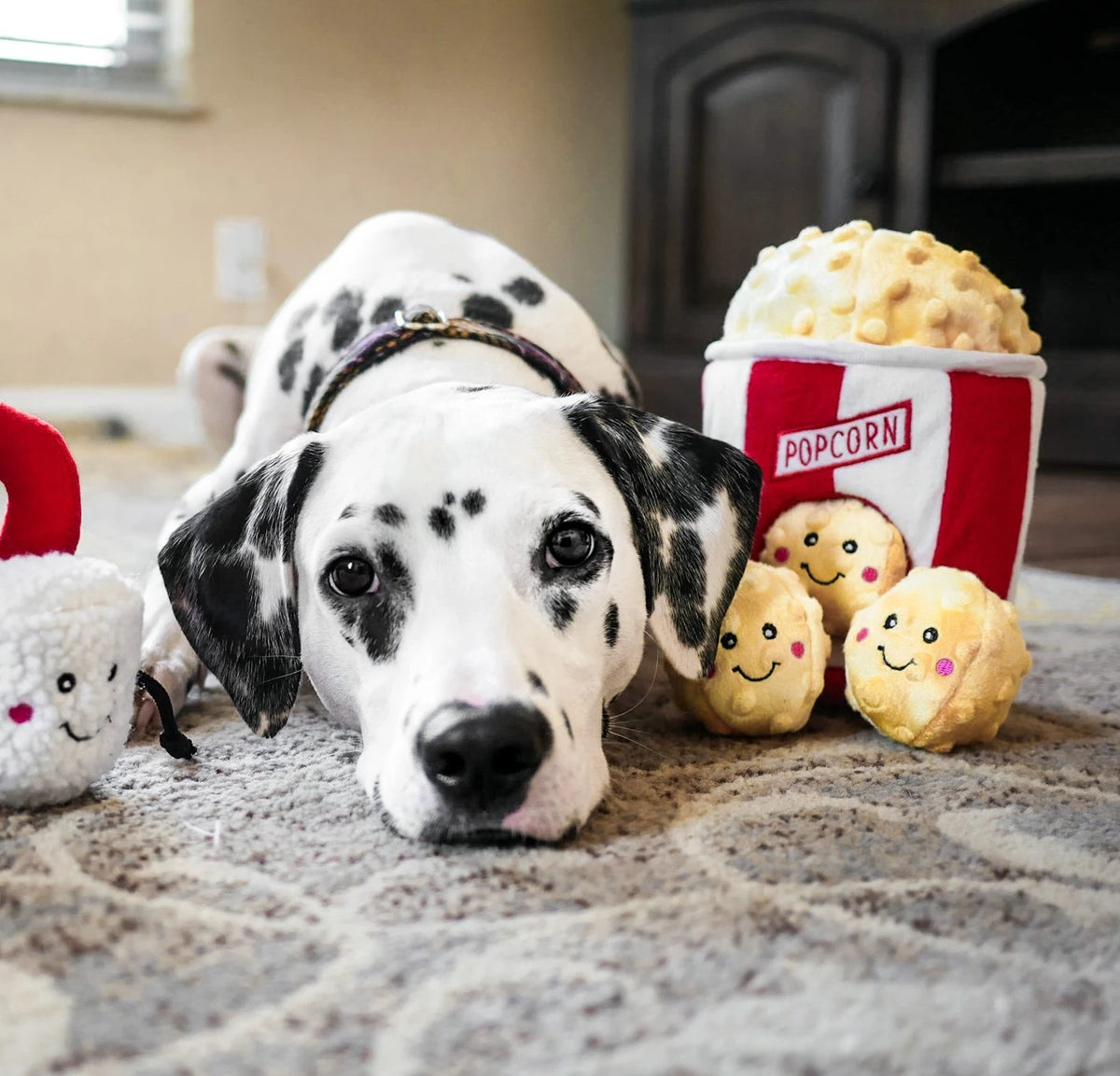 Dalmatian lying on carpet with a Zippy Paws Burrow popcorn bucket plush dog toy