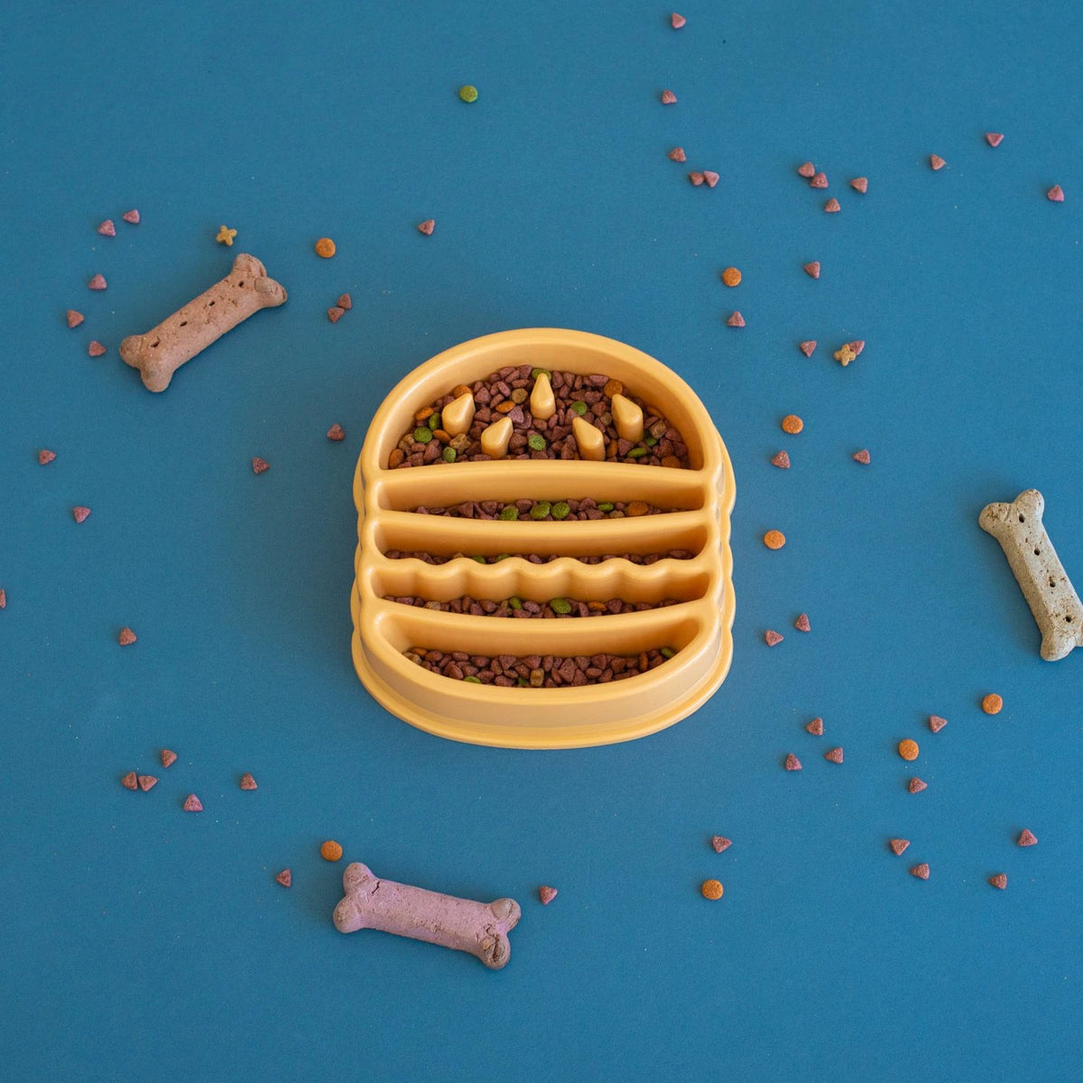 Zippy Paws hamburger-shaped slow feeder bowl filled with kibble on a blue backdrop