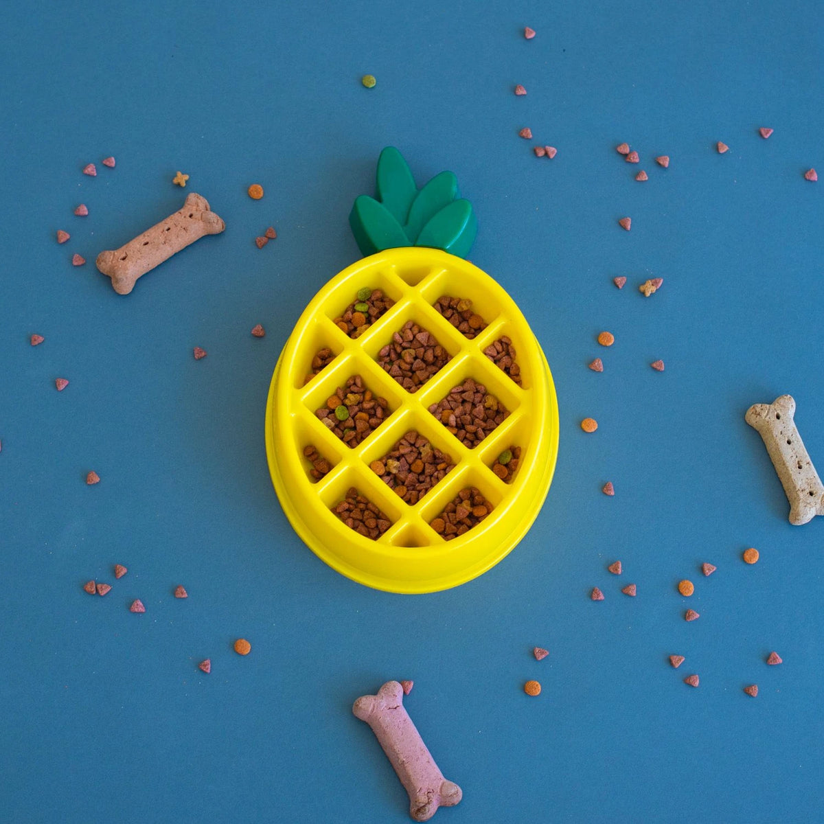Zippy Paws pineapple-shaped slow feeder bowl filled with kibble on a blue backdrop